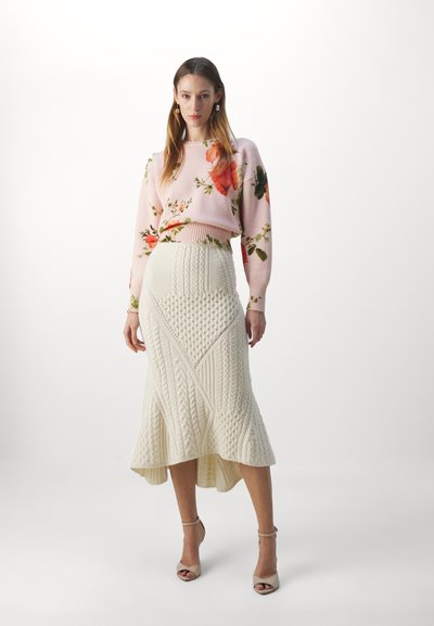 Light pink knitted sweater with floral pattern paired with a cream, textured midi skirt. Model wears beige ankle strap heels.