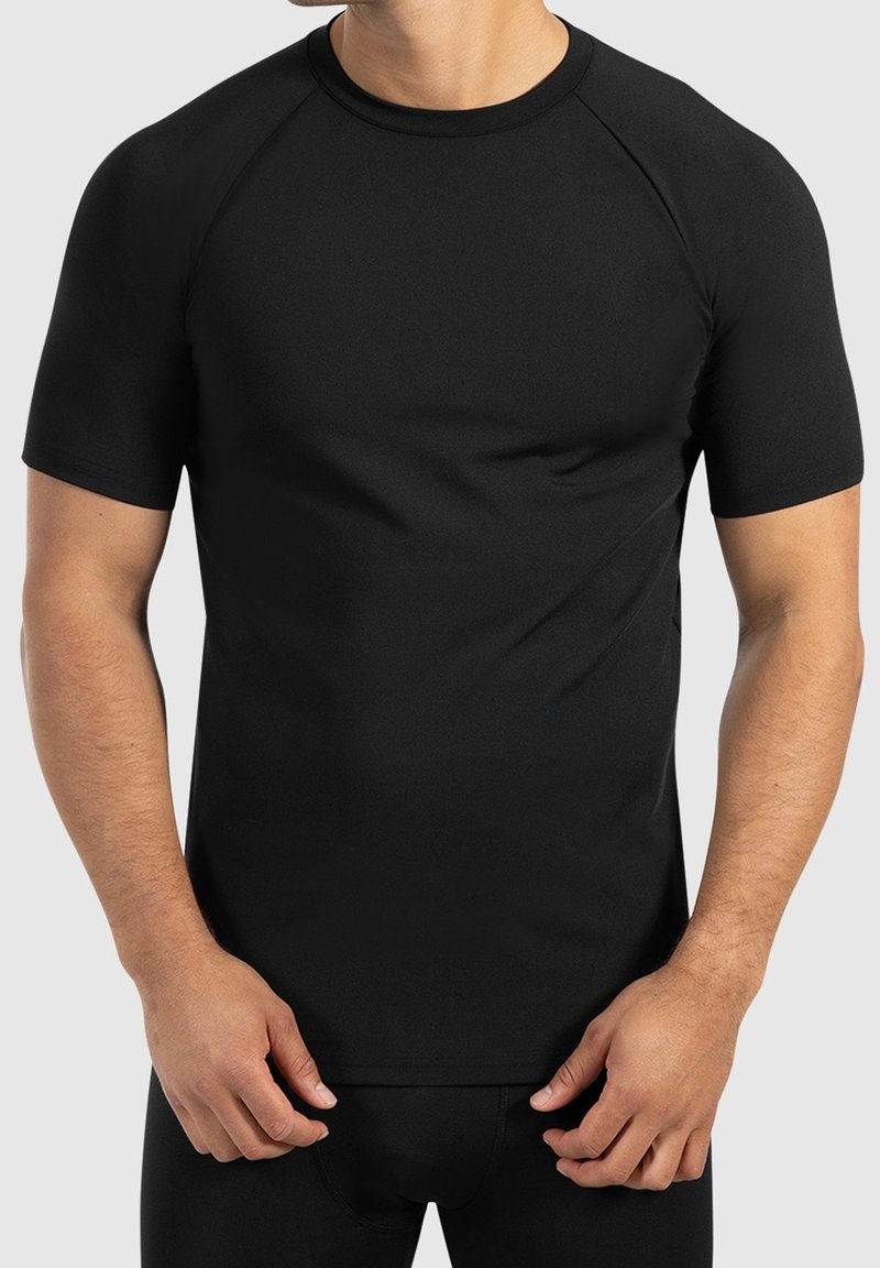 Homme portant un t-shirt de sport noir ajusté à manches courtes et un pantalon noir assorti sur un fond uni.