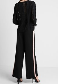 Schwarzes Spitzenoberteil mit strukturierten Streifen, kombiniert mit schwarzen, weit geschnittenen Hosen mit pinkfarbenen Seitenstreifen; elegantes Design und transparentes Gewebe.