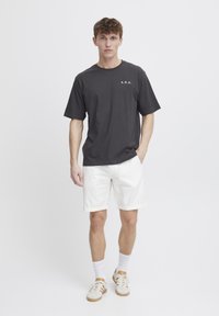 Mørkegrå bomulds T-shirt med "A.R.C." trykt på brystet, parret med hvide denim shorts og beige sneakers. En simpel, afslappet pasform.
