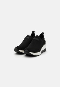 Sneaker slip-on nere in maglia con suola bianca, caratterizzate da una finitura testurizzata, colletto imbottito e una piccola etichetta con logo sul lato superiore.