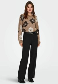 Suéter beige con patrón floral en blanco y negro, combinado con pantalones negros de talle alto y botines de tacón negro.
