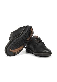 Zapatos de cuero negro con punta redonda, detalles marrones y una suela de goma texturizada con un patrón de dibujo profundo para mayor agarre.