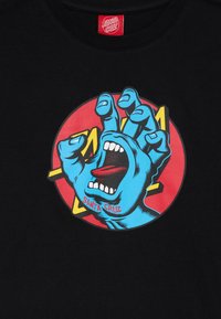 Schwarzes T-Shirt mit einem großen Grafikdesign einer blauen Hand mit offenem Mund auf einem roten runden Hintergrund, das ein gewagtes, cartoonhaftes Design zeigt.