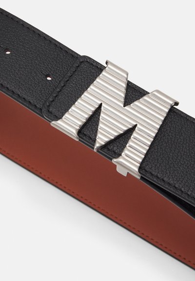 Svart lærbelte med en stor metallbuckle i form av et "M" med vertikale riller. Belte har kontrastrød innvendig fôr og kontraststing.