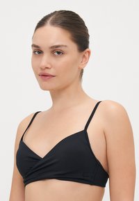 Black bikini top with a wrap design, featuring thin straps, soft texture, and a fitted shape. Includes a fabric tag on the side.