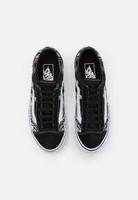 Baskets noires et blanches avec un imprimé bandana sur les côtés, un bout en suède noir texturé et une semelle en caoutchouc blanche avec des lacets noirs.