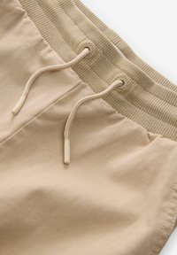 Beige tygshorts med ribbad elastisk midja och dragsko. Slät textur med en enkel design och inga synliga mönster eller detaljer.