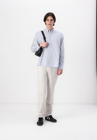 Camisa de rayas de manga larga en azul claro y blanco, combinada con pantalones beiges y zapatillas negras. Bolso negro con correa de hombro.