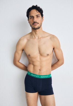 Marineblauwe boxershorts met een groene elastische tailleband waarop herhaaldelijk de tekst "GANT" staat. Zachte, gladde stoftextuur. Strak ontwerp.