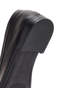 Tacco di scarpa in pelle nera con forma arrotondata, superficie texturizzata e multiple scanalature orizzontali vicino alla parte superiore. Suola in gomma con dettagli del logo.