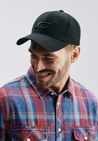 Czarna czapka z haftowanym logo, wykonana z tkaniny, w połączeniu z czerwoną i niebieską koszulą w kratę z kołnierzykiem na guziki i kieszeniami na piersi.