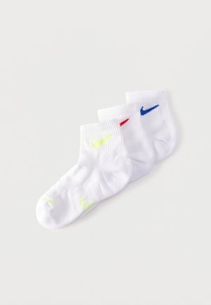 Tres calcetines blancos hasta el tobillo dispuestos superpuestos, cada uno con un logo diferente de Nike Swoosh en amarillo, rojo y azul.