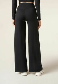 Svarta vida byxor med hög midja, tillverkade av mjukt tyg, med en enkel design och tillsammans med vita sneakers för kontrast.