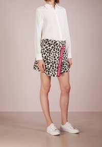 Bílé dlouhé tričko s dlouhým rukávem v kombinaci s mini sukní s leopardím potiskem, na které je červená nášivka "PINKO". Model má na sobě bílé tenisky.