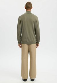 Pull en maille verte avec col et manches longues, associé à un pantalon beige ample, vu de dos sur un fond blanc.