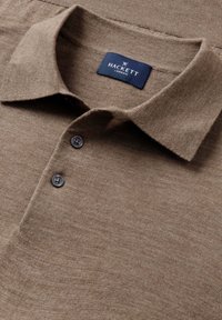 Bruine polo t-shirt met een kraag, een placket met twee knopen en een gestructureerde stof, met een label met de tekst "HACKETT LONDON."
