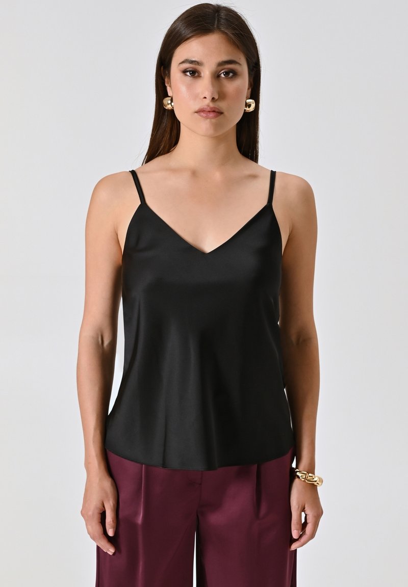 Camicetta in satin nera con scollatura a V, sottili spalline regolabili e una texture liscia. Abbinata a pantaloni bordeaux a vita alta.