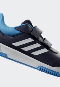 Baskets de sport bleues et marine avec une tige texturée, logo à trois bandes blanches, sangles Velcro et semelle en caoutchouc avec motifs d'adhérence.