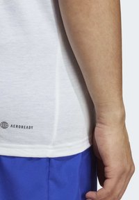 Witte sportshirt gemaakt van ademend materiaal, met een logo "AEROREADY" aan de onderkant, gecombineerd met blauwe shorts.