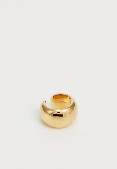 Bague dorée avec un design lisse et arrondi et une découpe semi-circulaire. Présente une texture polie et un logo en relief sur le côté intérieur.