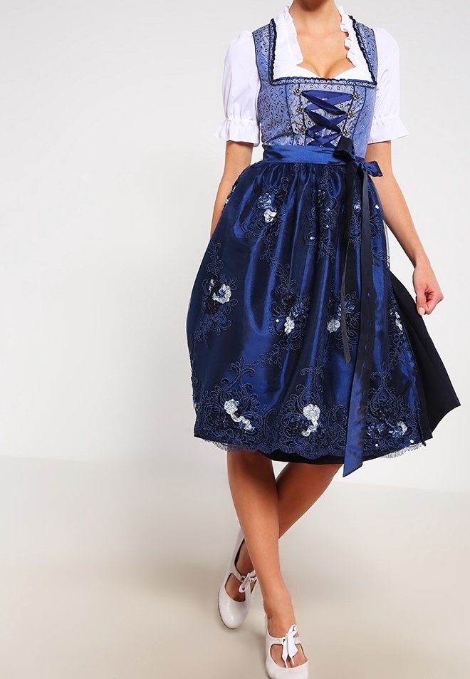 Dirndl en satin bleu marine avec broderies florales, corsage à lacets, manches de blouse blanche et une ceinture assortie en satin. À porter avec des chaussures de couleur claire.