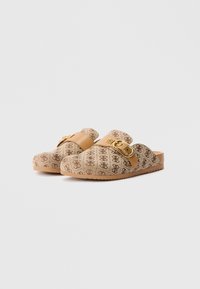 Paar beige instapslippers met bruin monogrampatroon, tan leren band en decoratieve gouden gesp op een witte achtergrond.