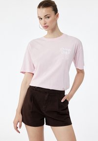 Jasnoróżowa bawełniana koszulka z krótkim rękawem z grafiką "Dream" i kokardką. W komplecie z ciemnobrązowymi szortami o gładkiej fakturze, casualowy styl.