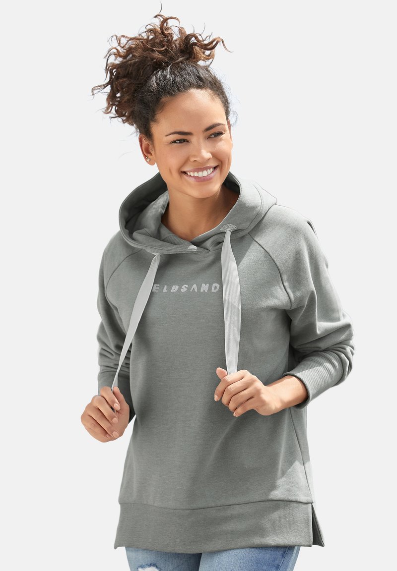 Felpa grigia chiara con cappuccio e cordini, maniche raglan e un logo sottile. Tessuto morbido con orlo allungato e fessure laterali per il comfort.