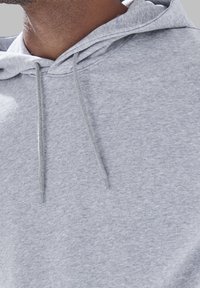 Sweatshirt gris avec une texture douce, des cordons de serrage ajustables et une poche avant. Design minimaliste axé sur le confort et la praticité.