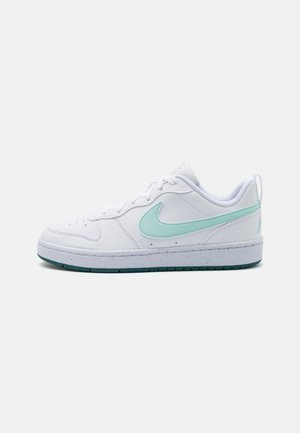 Baskets basses blanches avec un swoosh Nike vert menthe clair et une semelle blanche tachetée sur un fond uni.