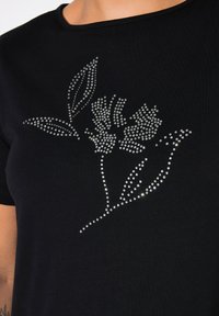 Camiseta negra de manga corta con un diseño floral creado con brillantes rhinestones, destacando hojas y flores. Textura de tela suave.