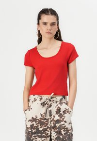 Haut rouge à manches courtes et décolleté rond en coton. Associé à un pantalon beige avec des motifs abstraits marron et une ceinture élastique.