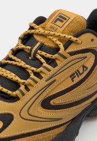 Fila sneaker featuring a black mesh upper with tan leather accents, yellow laces, a padded collar, and a logo patch on the tongue.
