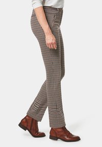 Pantaloni con motivo a capelli di cane in marrone e beige, realizzati in tessuto testurizzato, design aderente con tasche laterali, abbinati a stivaletti marroni alla caviglia.