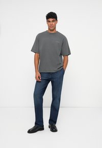 T-shirt grigia in cotone con maniche corte e scollatura rotonda, abbinata a jeans in denim blu e mocassini neri. Design semplice, vestibilità casual.