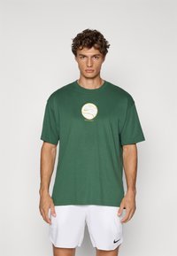 Grøn bomulds t-shirt med rund halsudskæring, korte ærmer, med et gult og hvidt Nike-logo grafik i midten.