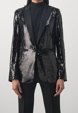 Blazer negro con lentejuelas y solapas de satén; corte ajustado con bolsillos delanteros y una superficie texturizada y brillante que refleja la luz.