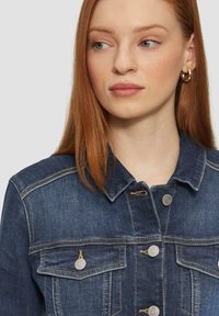 Donker denim jacket met een klassieke kraag, twee borstzakken en zilverkleurige knoophardware met contrasterende stiksels. Glad textuur.