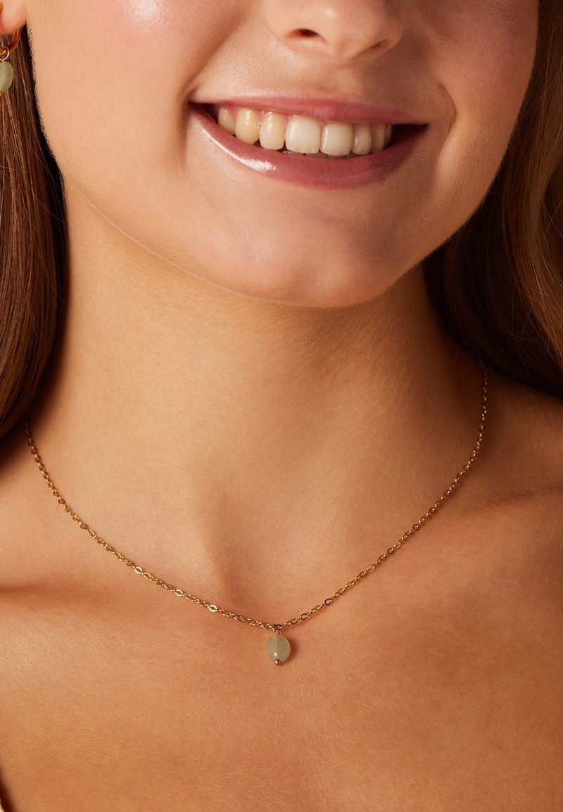 Collar de cadena de oro con un pequeño colgante ovalado. El colgante es una piedra verde clara translúcida, que resalta la delicada artesanía.