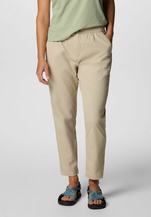 Beige, leichte Hose mit elastischem Bund, taillierter Schnitt und zwei Seitentaschen, kombiniert mit schwarz-blauen Sandalen.