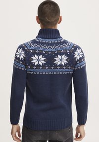Sötétkék kötött pulóver magas gallérral, fehér és világoskék hópehely mintákkal, bordás mandzsettával és aljjal.