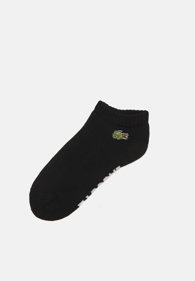 Chaussette noire de cheville en mélange de coton, avec un logo de crocodile vert et des lettres blanches sur le côté. Bord ribbed en haut.