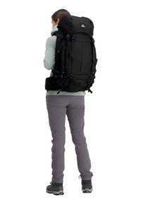 Zwarte wandelaarsrugzak met verstelbare banden, bovenklep en meerdere vakken; gedragen door een persoon in een lichte jas en grijze broek.