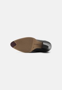 Black shoe sole with textured grip, pointed toe, and flexible rubber heel. Features brown rubber base with horizontal lines and logo detail.