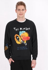 Sweatshirt negru cu texte colorate și desene grafice. Mâneci lungi cu un model de accent pe mâna stângă. Croială casual.