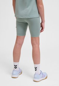 Ljust gröna cykelshorts i kombination med en avslappnad topp; vita strumpor med svart chevronmönster; lavendelfärgade träningsskor med beige sulor.