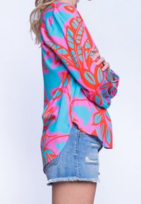 Chemise à manches longues multicolore avec un motif floral audacieux en rose, rouge et turquoise, associée à un short en jean déchiré.