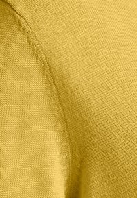 Neulottu neulepaita kirkkaankeltaisesta kankaasta. Siinä on sileä rakenne ja näkyvät ompelusaumat.