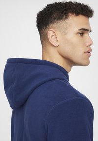 Felpa con cappuccio in pile blu navy con una texture morbida, dotata di cappuccio e design delle spalle senza cuciture. Linee pulite e dettagli minimi.